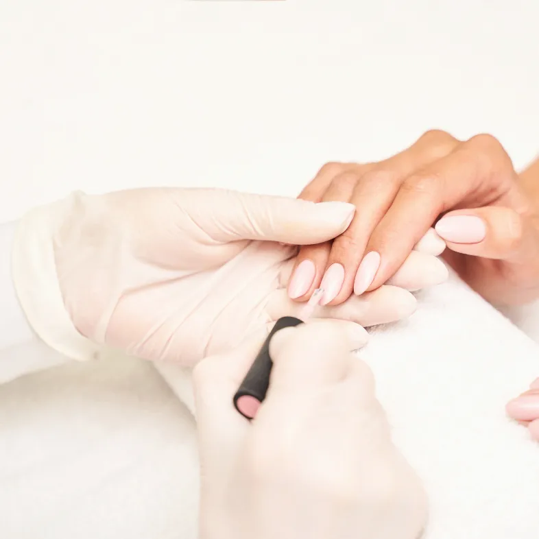 Pflegender Auftrag von hellem Nagellack bei einer Maniküre
